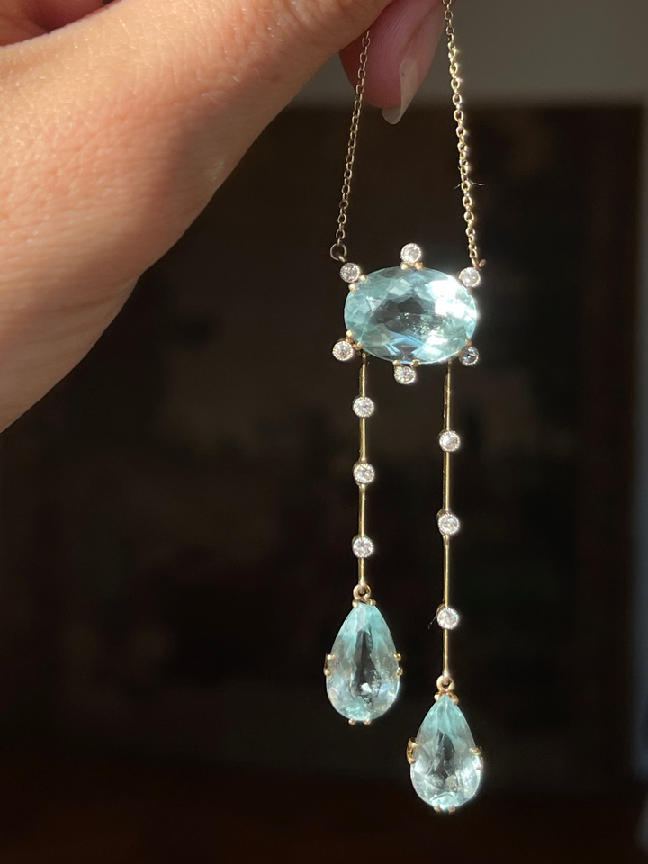 An aquamarine and diamond necklace held before a dark toille.