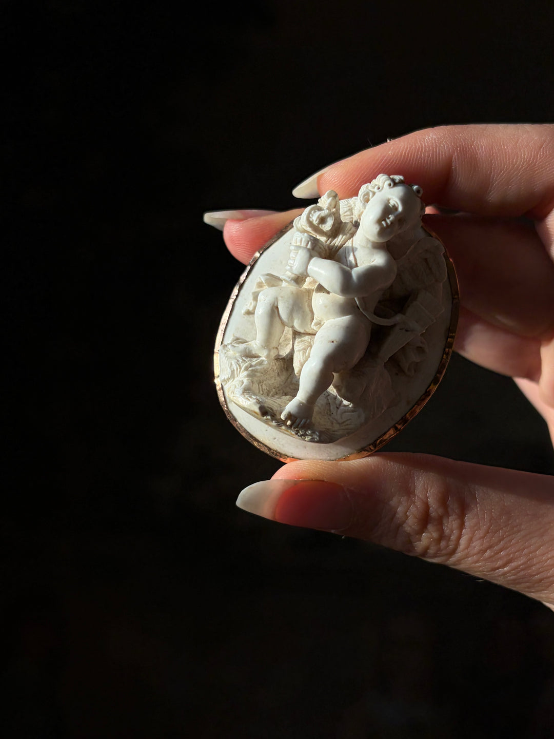 Tilted view of the Grand Tour lava Cupid cameo, showing its deep carving and oval gold setting.