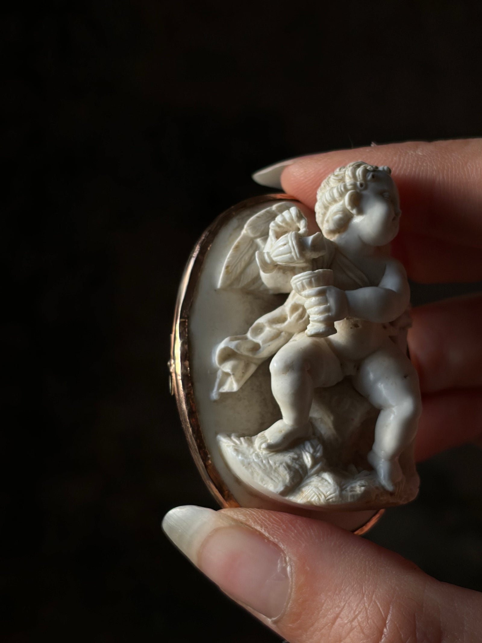 Angled view of the high relief lava Cupid cameo, showing the wine jug, goblet and carved wings.