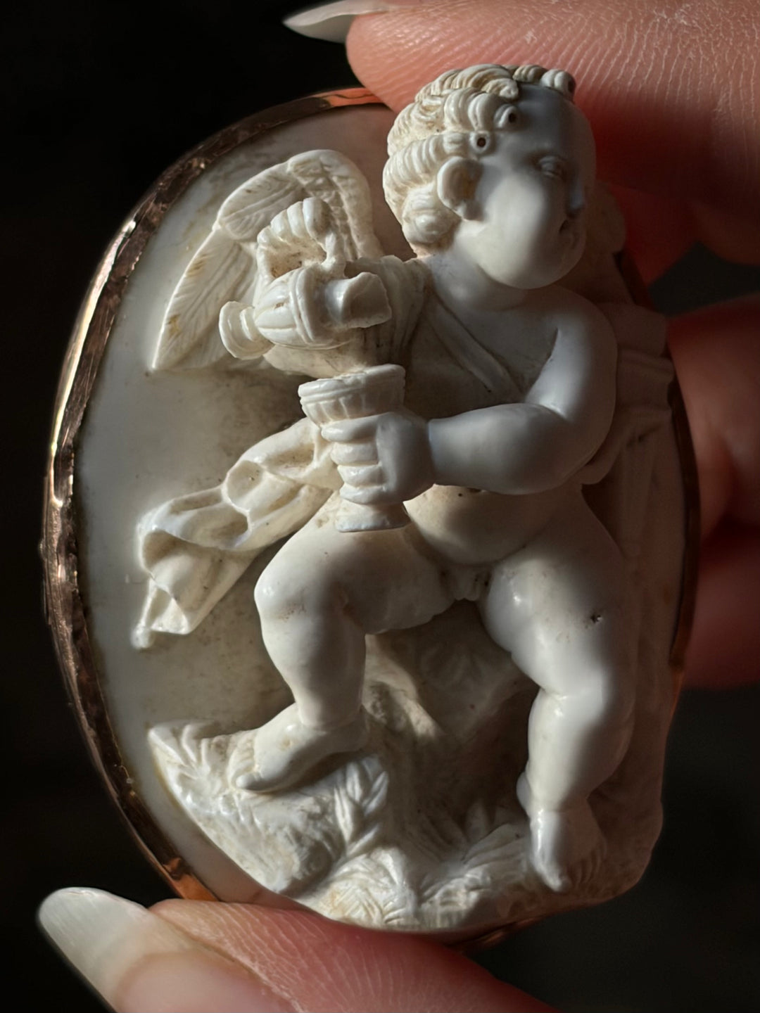 Close-up of Cupid pouring wine in the antique lava cameo, showing carved curls and damage to the jug