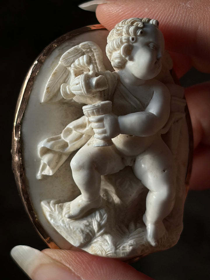 Close-up of Cupid pouring wine in the antique lava cameo, showing carved curls and damage to the jug