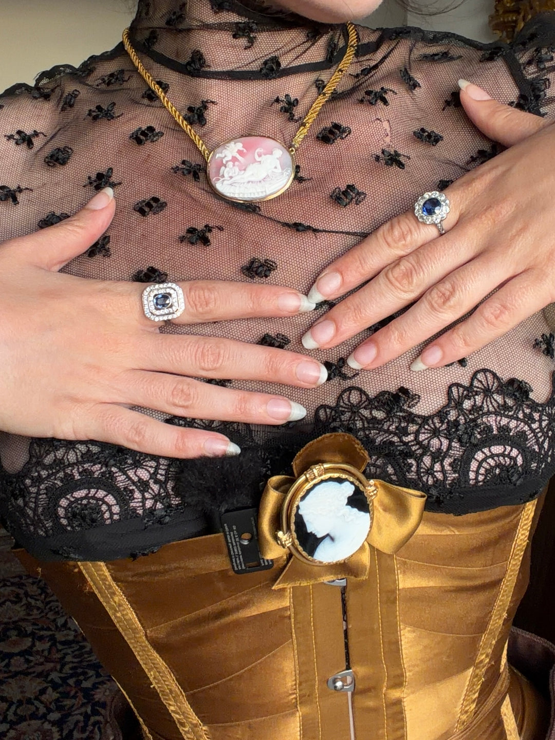 Antique cameo jewellery styled with black lace and a gold corset, including a pink cameo pendant and profile brooch.